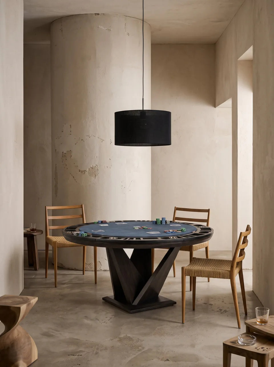 Table de poker ronde à pied en V et tapis bleu nuit, trois chaises en bois, colonne de béton et suspension noire