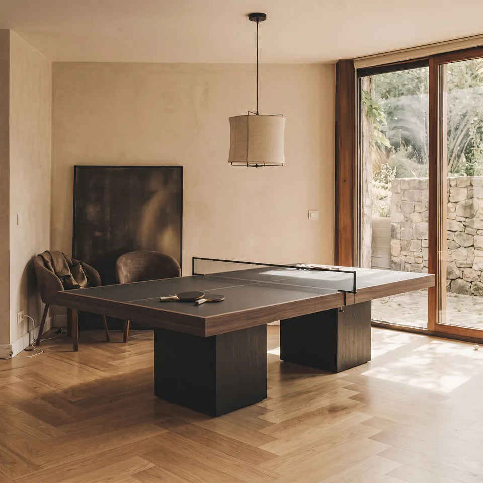 Table de ping-pong à cadre en bois foncé sur deux blocs noirs, parquet à chevrons, baie vitrée sur un jardin
